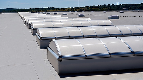 Rows of Lichtband B units by roda on a flat industrial roof under sunny conditions.