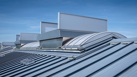 Lichtband B by roda with ventilation units on a metal roof under a blue sky.