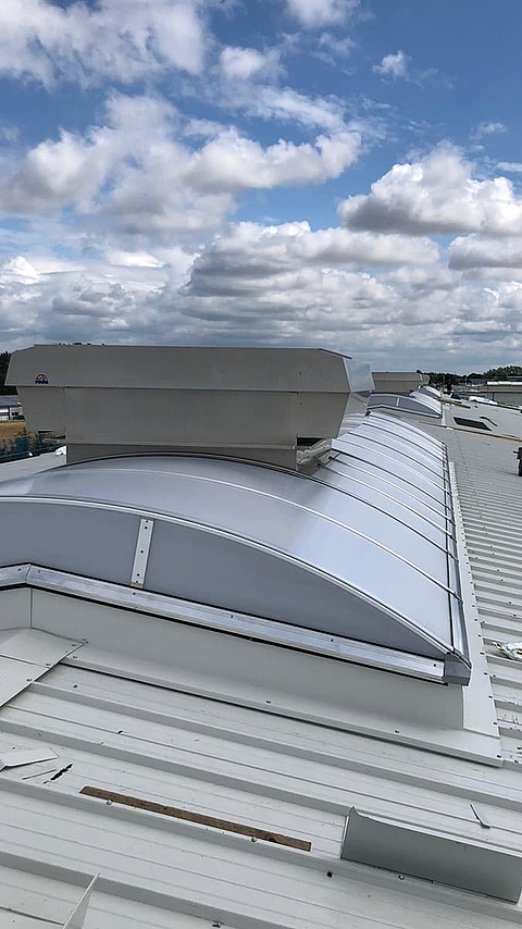 Lichtband B by roda with integrated ventilation unit on industrial roof under cloudy sky.