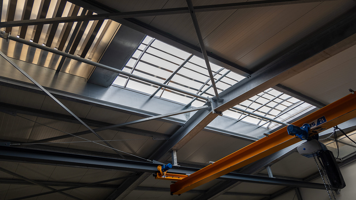 Blick von innen auf ein Industriedach mit integrierten Lichtbändern und Stahlkonstruktion.