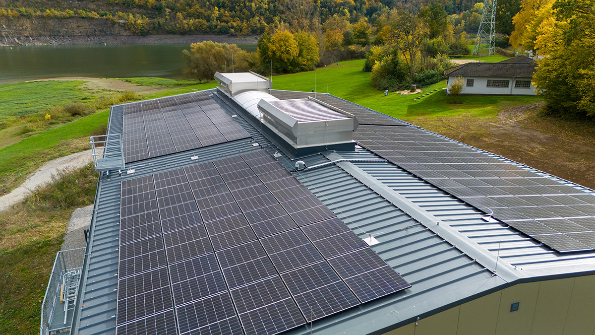 Industriedach mit Solarpaneelen und Lichtband, umgeben von grüner Landschaft.